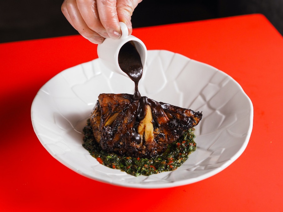  A hand with a see-through glove pouring some sauce on top of a juicy piece of meat. 