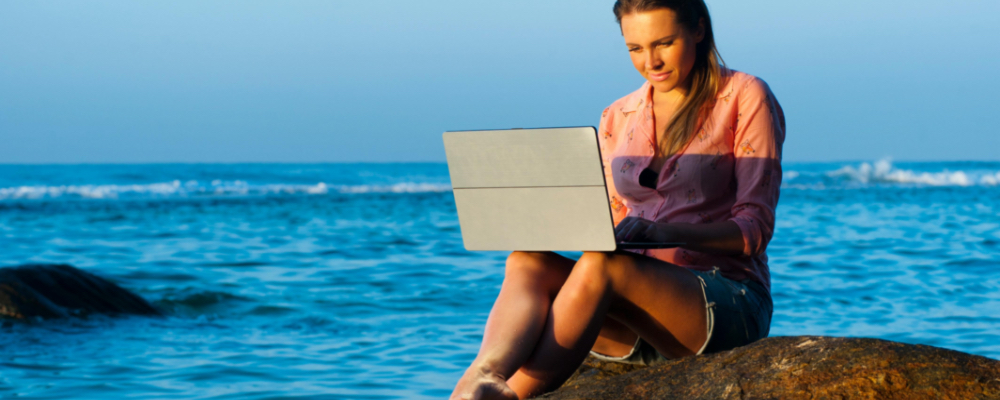 Woman with laptop on rocks by ocean