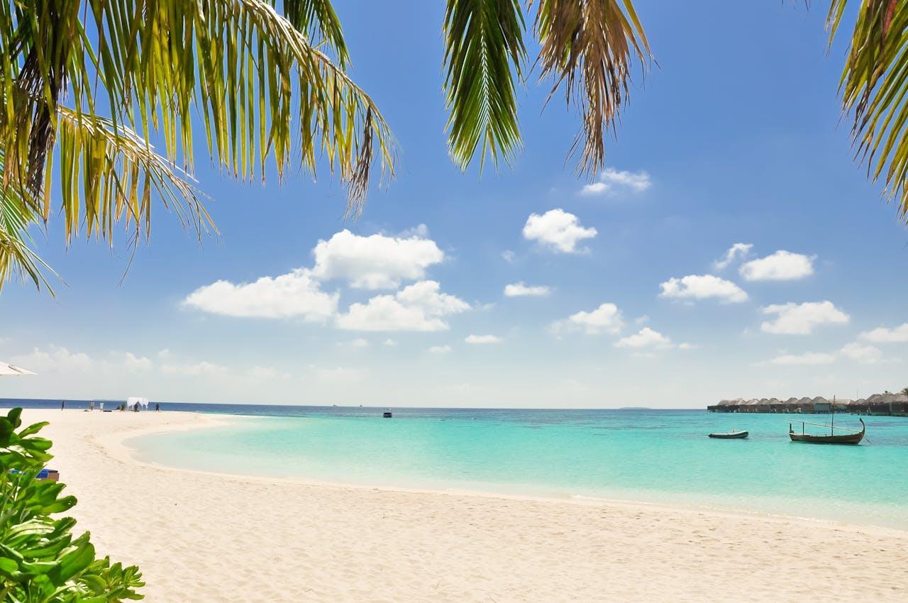 A picture of a sand beach with two boats in the distance. 
